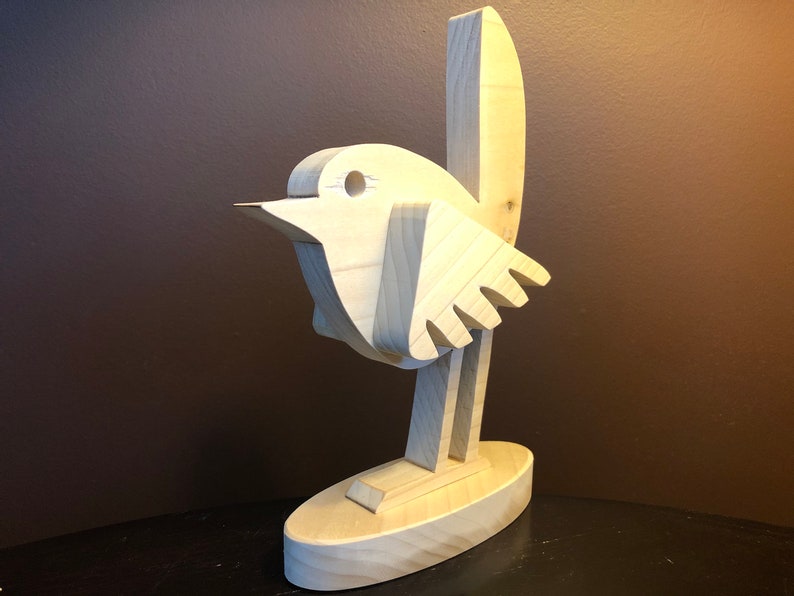 K&ouml;nnte beinhalten: Eine Holzskulptur eines Vogels mit einem einfachen, abstrakten Design. Der Vogel steht auf einem Sockel und hat einen langen, d&uuml;nnen Hals und einen kleinen Kopf. Die Skulptur ist aus hellem Holz gefertigt und hat eine nat&uuml;rliche Oberfl&auml;che.