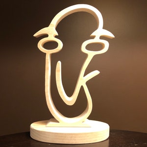 May include: A wooden sculpture of a stylized face with a large, open mouth and eyes. The sculpture is on a wooden base.