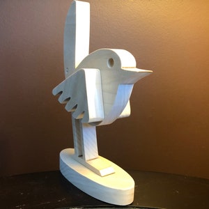 K&ouml;nnte beinhalten: Eine wei&szlig;e Holzvogelskulptur mit langem Schwanz und Schnabel. Der Vogel steht auf einem kleinen ovalen Sockel.