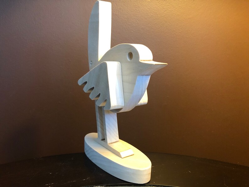 K&ouml;nnte beinhalten: Eine wei&szlig;e Holzvogelskulptur mit langem Schwanz und Schnabel. Der Vogel steht auf einem kleinen ovalen Sockel.