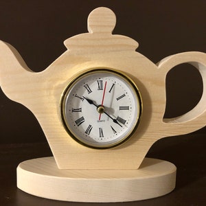 May include: A wooden teapot shaped clock with a white face and black hands. The clock has Roman numerals and says "Quartz" at the bottom. The teapot is sitting on a wooden base.