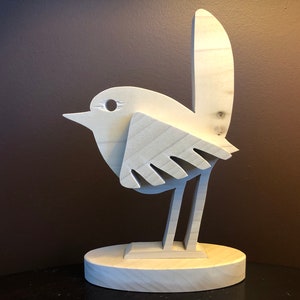K&ouml;nnte beinhalten: Eine Holzskulptur eines Vogels mit einem einfachen, abstrakten Design. Der Vogel steht auf einem Sockel und hat einen langen Schwanz.