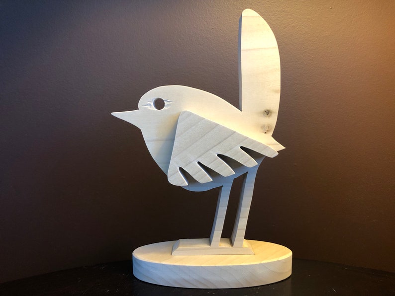 K&ouml;nnte beinhalten: Eine Holzskulptur eines Vogels mit einem einfachen, abstrakten Design. Der Vogel steht auf einem Sockel und hat einen langen Schwanz.