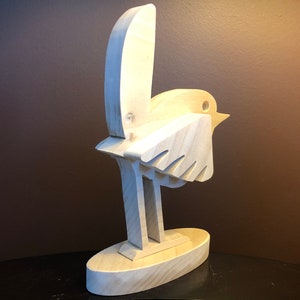 K&ouml;nnte beinhalten: Eine Holzskulptur eines Vogels mit einem einfachen, abstrakten Design. Der Vogel steht auf einem Sockel und hat seine Fl&uuml;gel ausgebreitet.