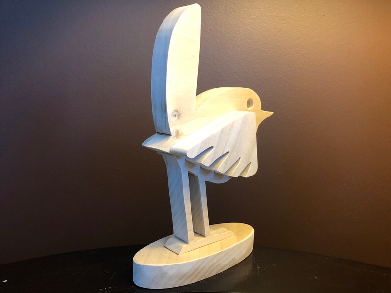 K&ouml;nnte beinhalten: Eine Holzskulptur eines Vogels mit einem einfachen, abstrakten Design. Der Vogel steht auf einem Sockel und hat seine Fl&uuml;gel ausgebreitet.