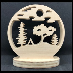 May include: A wooden cutout of a forest scene with a tent, trees, and a moon. The cutout is mounted on a wooden base.