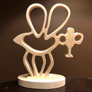 May include: A wooden cutout of a bee with wings, a body, and legs. The bee is standing on a round wooden base.