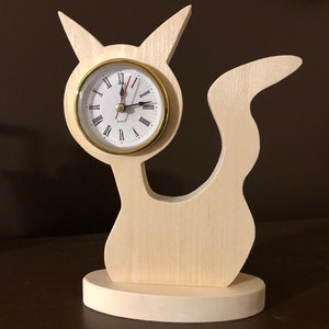 May include: A wooden cat-shaped clock with a white face and gold trim. The clock has Roman numeral hour markers and black hands.