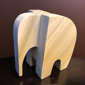 May include: A wooden elephant sculpture made of two pieces of wood. The elephant is light brown and has a smooth finish.