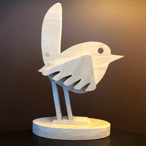 K&ouml;nnte beinhalten: Eine Holzskulptur eines Vogels mit einem einfachen, stilisierten Design. Der Vogel steht auf einem runden Sockel und hat einen langen, d&uuml;nnen Schnabel. Die Skulptur ist aus hellem Holz gefertigt und hat eine nat&uuml;rliche Oberfl&auml;che.