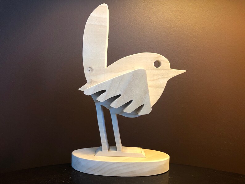 K&ouml;nnte beinhalten: Eine Holzskulptur eines Vogels mit einem einfachen, stilisierten Design. Der Vogel steht auf einem runden Sockel und hat einen langen, d&uuml;nnen Schnabel. Die Skulptur ist aus hellem Holz gefertigt und hat eine nat&uuml;rliche Oberfl&auml;che.