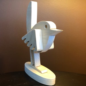 K&ouml;nnte beinhalten: Eine Holzskulptur eines Vogels mit einem einfachen, abstrakten Design. Der Vogel steht auf einem Sockel und hat seine Fl&uuml;gel ausgebreitet.