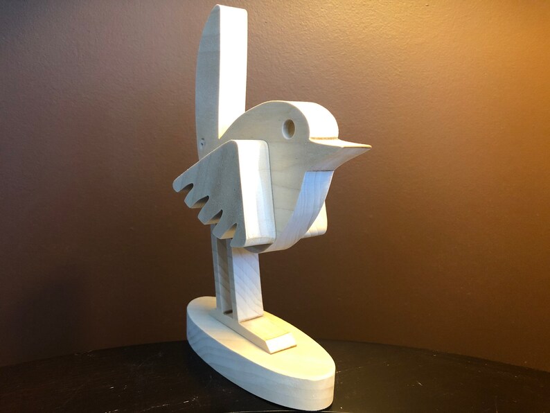 K&ouml;nnte beinhalten: Eine Holzskulptur eines Vogels mit einem einfachen, abstrakten Design. Der Vogel steht auf einem Sockel und hat seine Fl&uuml;gel ausgebreitet.