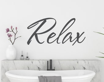 May include: A white bathtub with a grey towel on the edge. The wall behind the tub has a black cursive word "Relax" on it.