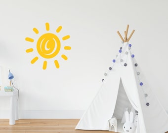 May include: A yellow sun wall decal with a simple, hand-drawn design. The decal is on a white wall next to a white teepee tent with blue and silver string lights.