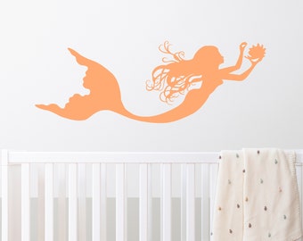 May include: A peach-colored mermaid silhouette wall decal with long flowing hair and a seashell in her hand.