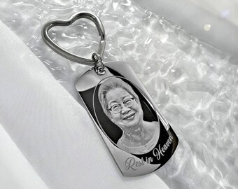 May include: Silver keychain with a heart-shaped ring and a rectangular tag. The tag has a black and white photo of a person and the words "Rest in Heaven" engraved on it.
