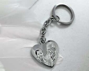 May include: A silver heart-shaped keychain with a photo of a baby and an older person engraved on it.