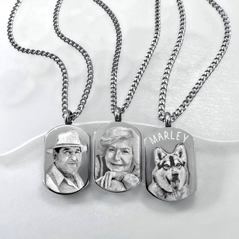 May include: Three stainless steel dog tag necklaces with engraved portraits. One features a man in a hat, another an older woman, and the third a dog with the name "MARLEY". Each tag hangs from a silver chain.