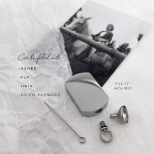 May include: A silver-colored, rectangular cremation urn with a rounded top, a small funnel, and a fill kit. The text "Can be filled with: ASHES, FUR, HAIR, DRIED FLOWERS" is visible. A black and white photo of a person riding a horse is in the background.