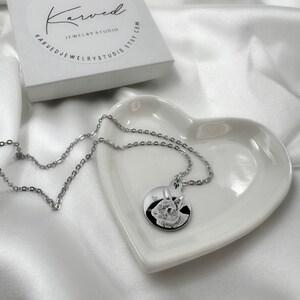 Op de afbeelding: Een zilveren ketting met een ronde hanger met een zwart-wit foto van een konijn. De hanger ligt op een hartvormig schaaltje.