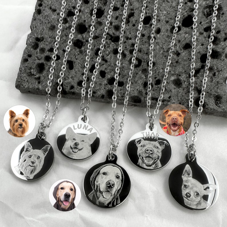 Op de afbeelding: Vijf zilveren kettingen met ronde hondenfoto-hangers. Elke hanger heeft een ander hondenras en heeft een gegraveerde naam. De namen zijn Luna, Thor en drie andere namen die niet zichtbaar zijn.