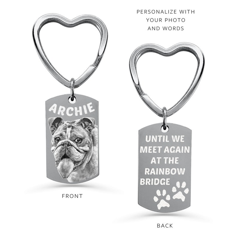 May include: Silver heart-shaped keyring with a rectangular tag. The front of the tag has a black and white photo of a bulldog with the name "Archie" printed above the photo. The back of the tag has the text "Until we meet again at the rainbow bridge" with two paw prints below the text.