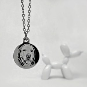 Op de afbeelding: Een zilveren ketting met een ronde hanger met een zwart-wit foto van een hondenkop.