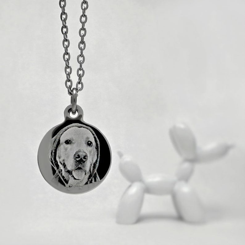 Op de afbeelding: Een zilveren ketting met een ronde hanger met een zwart-wit foto van een hondenkop.