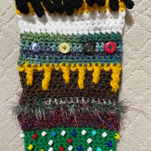 May include: A crocheted pouch with a variety of colors and textures, including black, white, brown, green, yellow, and purple. The pouch has a fringe trim, buttons, and beads.