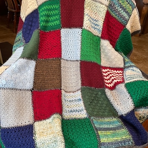 May include: A crocheted patchwork blanket with squares in various colors, including red, green, blue, brown, and white.