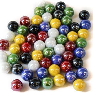 Puede incluir: Una colección de canicas de vidrio de colores en varios tonos de rojo, verde, azul, amarillo y negro. Las canicas están dispuestas en una pila sobre un fondo blanco.
