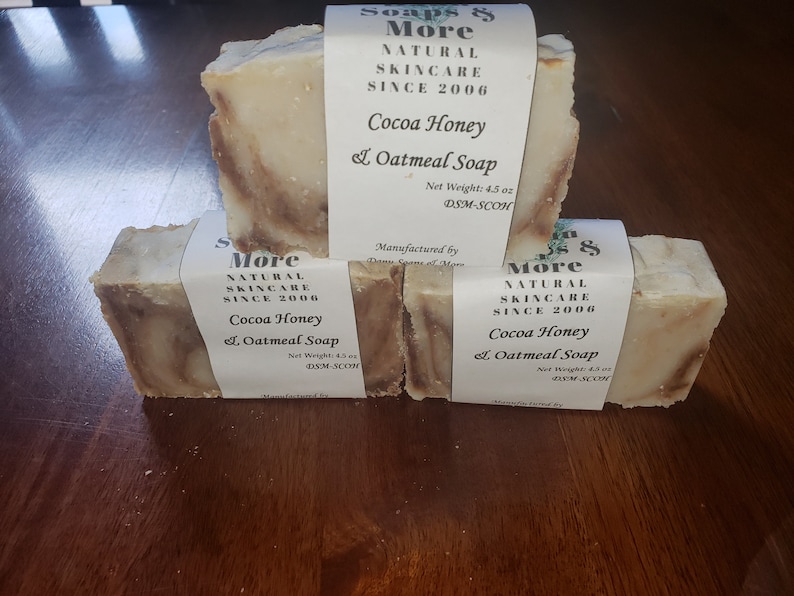 May include: Three bars of handmade soap with a brown and white swirl pattern. The soap is labeled "Soaps & More Natural Skincare Since 2006 Cocoa Honey & Oatmeal Soap" with a net weight of 4.5 oz.