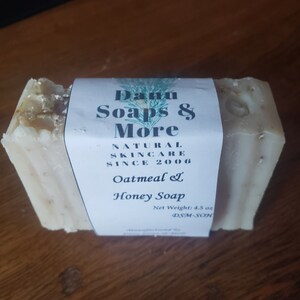 May include: A bar of white oatmeal and honey soap with a label that reads "Danu Soaps & More Natural Skincare Since 2006 Oatmeal & Honey Soap Net Weight: 4.5 oz DSM-SOH"