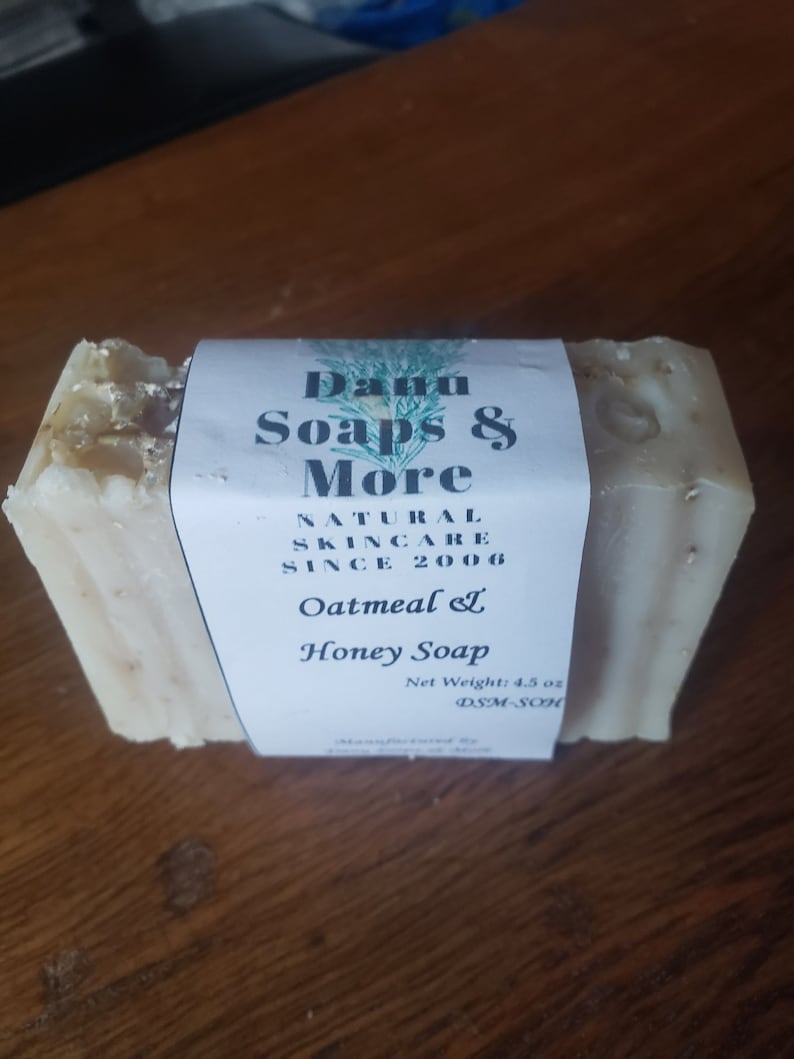May include: A bar of white oatmeal and honey soap with a label that reads "Danu Soaps & More Natural Skincare Since 2006 Oatmeal & Honey Soap Net Weight: 4.5 oz DSM-SOH"