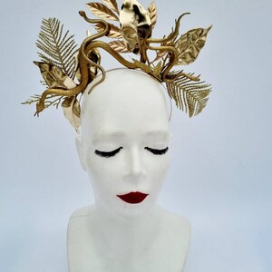May include: A gold headband with a snake and leaf design. The headband is made of metal and has a delicate, intricate design.