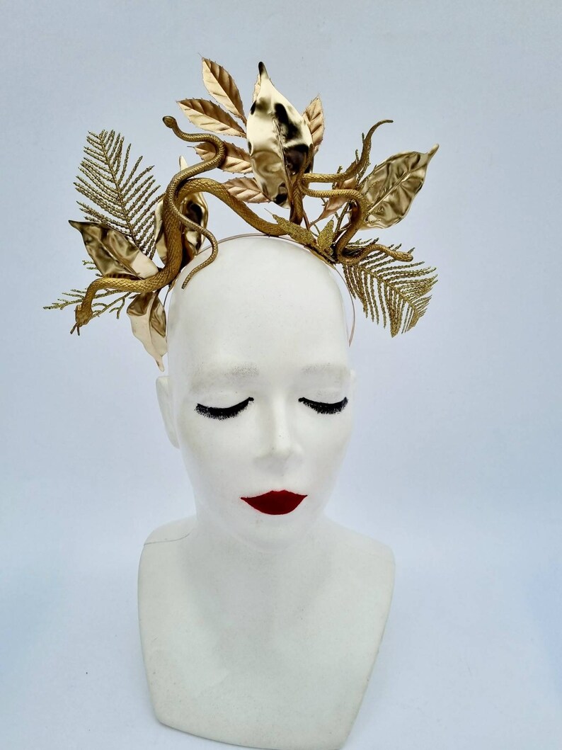 May include: A gold headband with a snake and leaf design. The headband is made of metal and has a delicate, intricate design.
