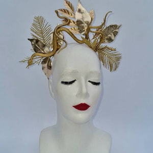 May include: A gold headband with a snake and leaves design. The headband is made of metal and has a shiny finish.