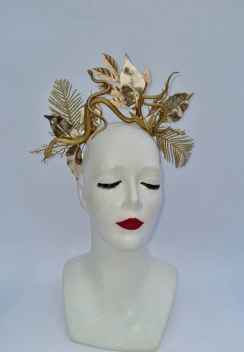 May include: A gold headband with a snake and leaves design. The headband is made of metal and has a shiny finish.