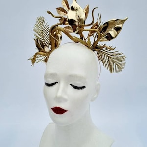 May include: A gold headband with a snake and leaf design. The headband is made of metal and has a shiny finish.