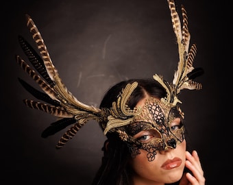 May include: A woman wearing a black and gold masquerade mask with feathers. The mask has a delicate lace design and is adorned with gold accents. The feathers are black and brown and are arranged in a fan shape.