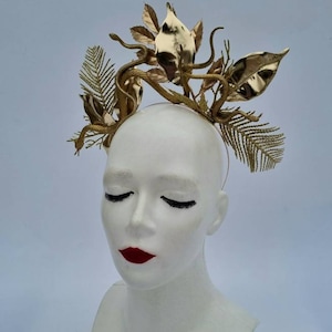 May include: A gold-colored headband with a snake and leaf design. The headband is made of metal and has a delicate, intricate design.