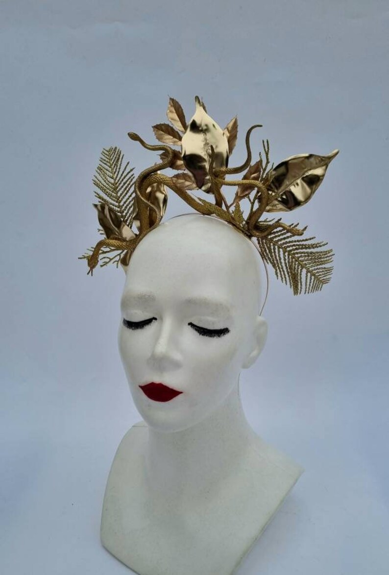 May include: A gold-colored headband with a snake and leaf design. The headband is made of metal and has a delicate, intricate design.