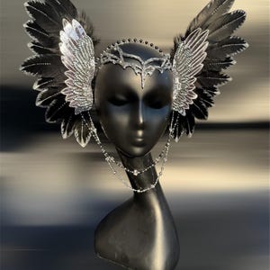 May include: A black and silver headpiece with feathers and a beaded chain. The headpiece is designed to look like wings.