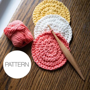 May include: Three crocheted cotton rounds in yellow, white, and pink, with a wooden crochet hook and a ball of pink yarn. The text "PATTERN" is written in a white circle.
