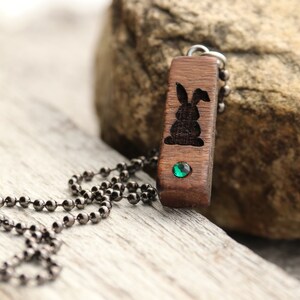 Peut inclure: Un collier avec un pendentif en bois sculpt&eacute; en forme de lapin et une pierre pr&eacute;cieuse verte. Le collier a une cha&icirc;ne en m&eacute;tal noir.
