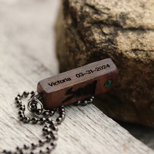 Peut inclure: Un collier avec un pendentif en bois et une cha&icirc;ne noire. Le pendentif est grav&eacute; avec le texte "Victoria 03-31-2024" et comporte une petite pierre pr&eacute;cieuse verte.