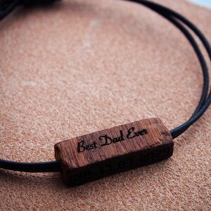 Peut inclure: Un bracelet en bois avec l'inscription gravée "Best Dad Ever". Le charm rectangulaire en bois est attaché à un cordon noir. La date "03.03.2024" est également gravée sur le charm. Le bracelet est un cadeau.