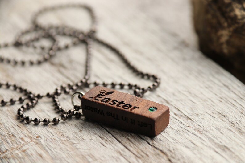 Peut inclure: Un collier avec un pendentif en bois et une pierre pr&eacute;cieuse verte. Le pendentif est grav&eacute; des mots "Let it be the Water" et "Easter".