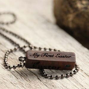Peut inclure: Un collier avec un pendentif en bois et une cha&icirc;ne noire. Le pendentif est grav&eacute; avec les mots "My First Easter".